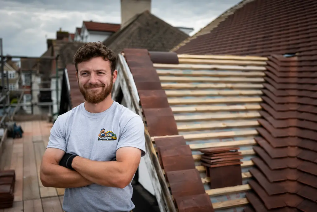 A smiling Local House Pros contractor standing on a roof ready to help with your project
